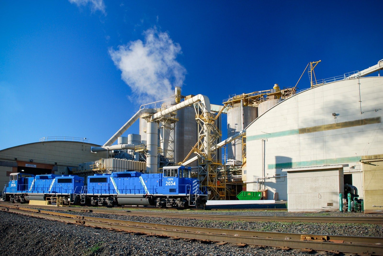 Two blue locomotives parked on rail tracks beside the silos and conveyors of the Roseburg lumber mill in Dillard, Oregon