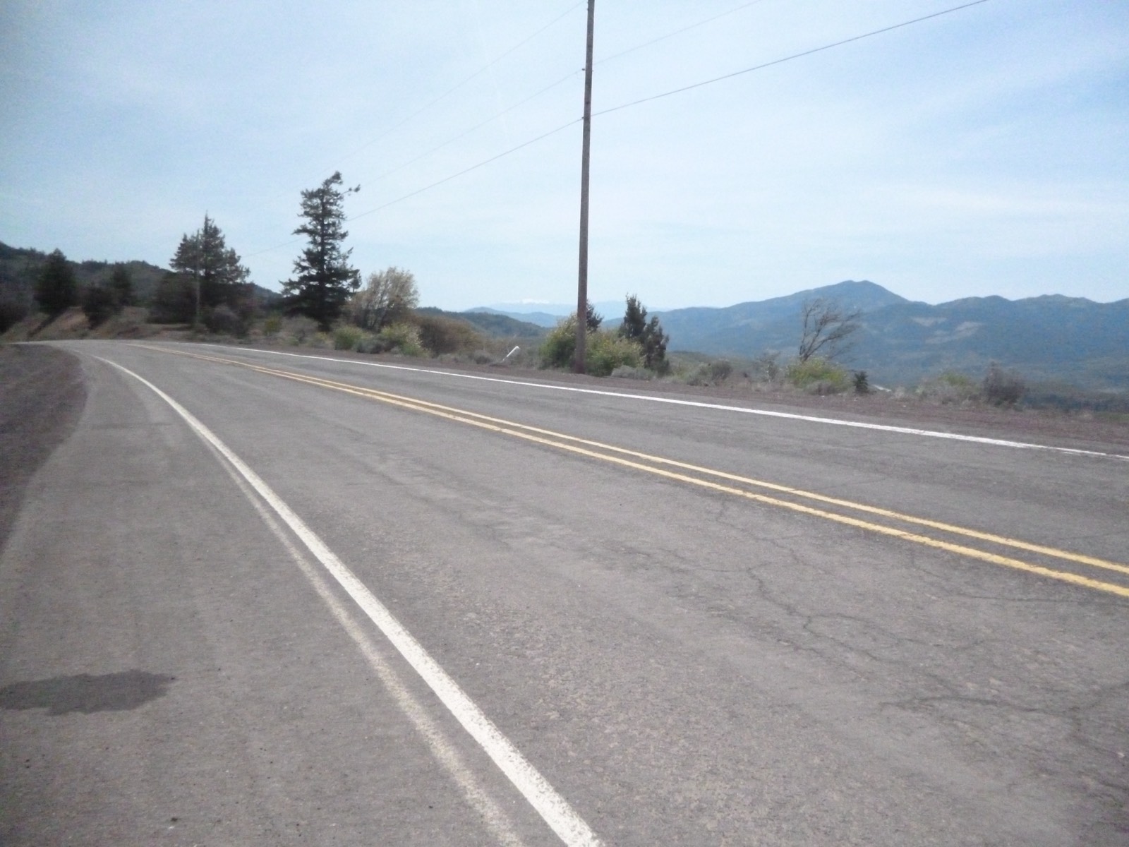 Empty two-lane stretch of old Highway 99 curving along Siskiyou Summit, with a wooden power pole and forested ridges in the haze beyond