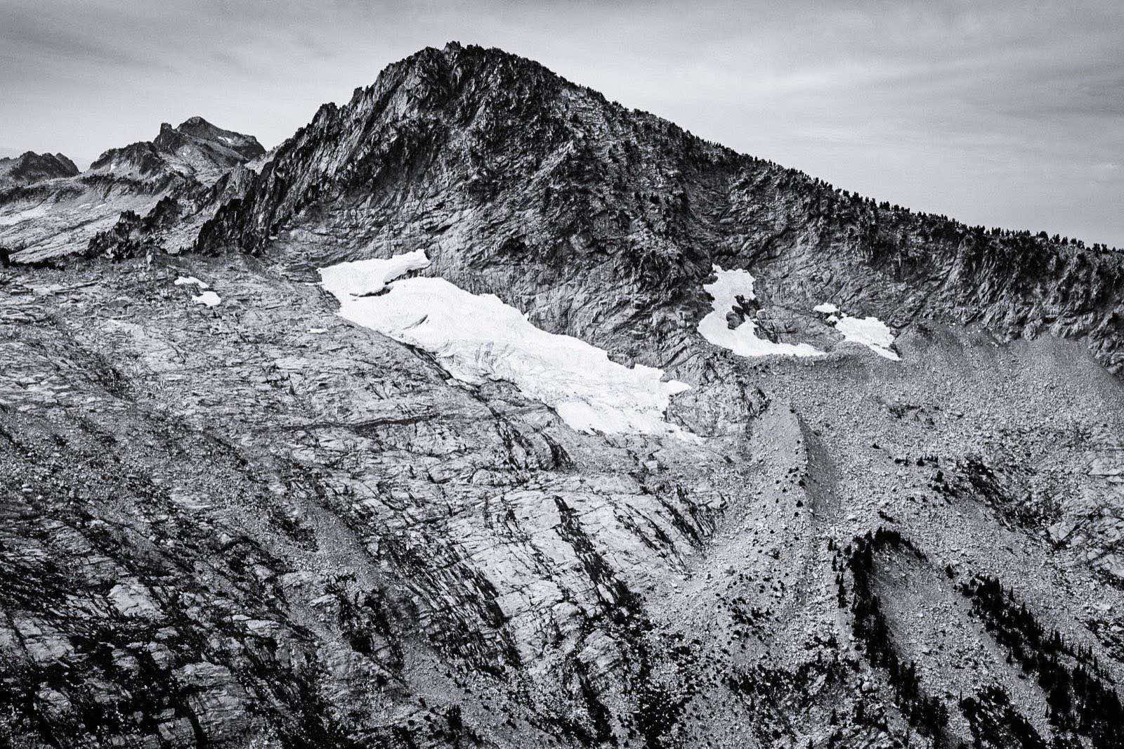 Black-and-white aerial photo of the rocky north face of Thompson Peak in the Trinity Alps with the small Grizzly Glacier clinging below the summit