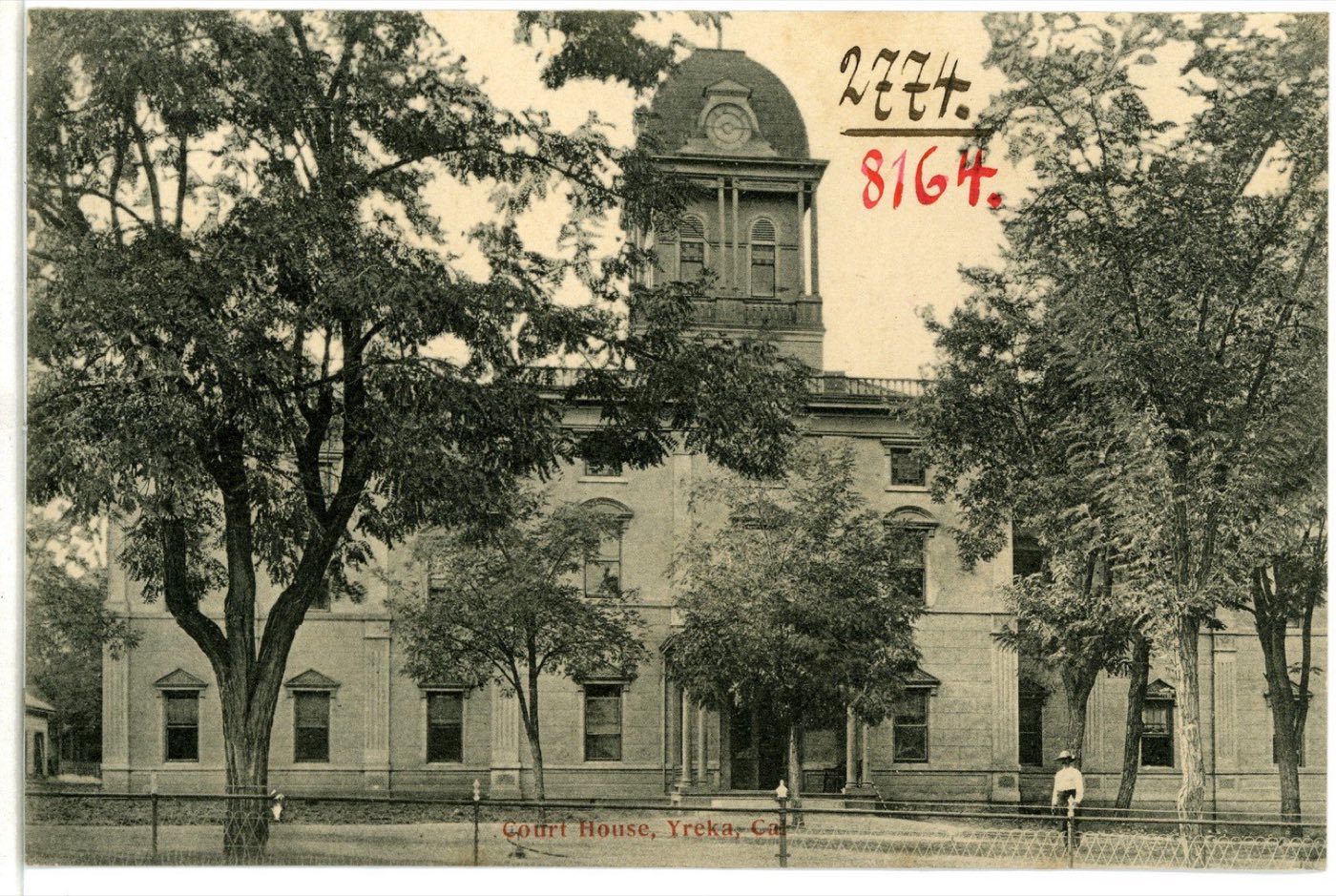 Black-and-white 1906 postcard of the Siskiyou County Court House in Yreka, a two-story stone building with a domed clock tower, framed by large trees